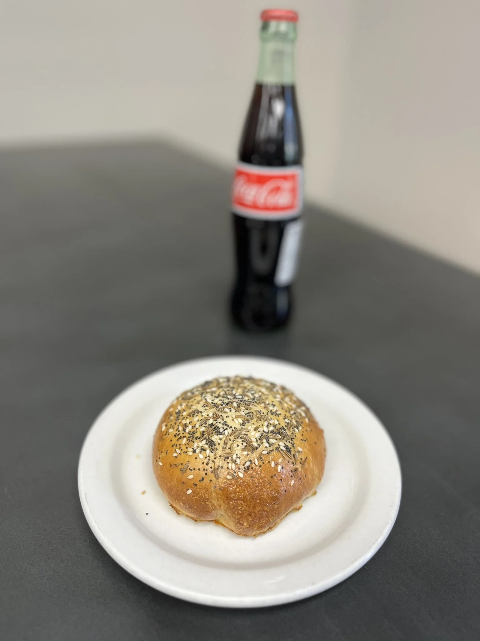Elm Creek Beef A poppy seed roll pastry on a white plate with a bottle of Coca-Cola in the background on a black table.