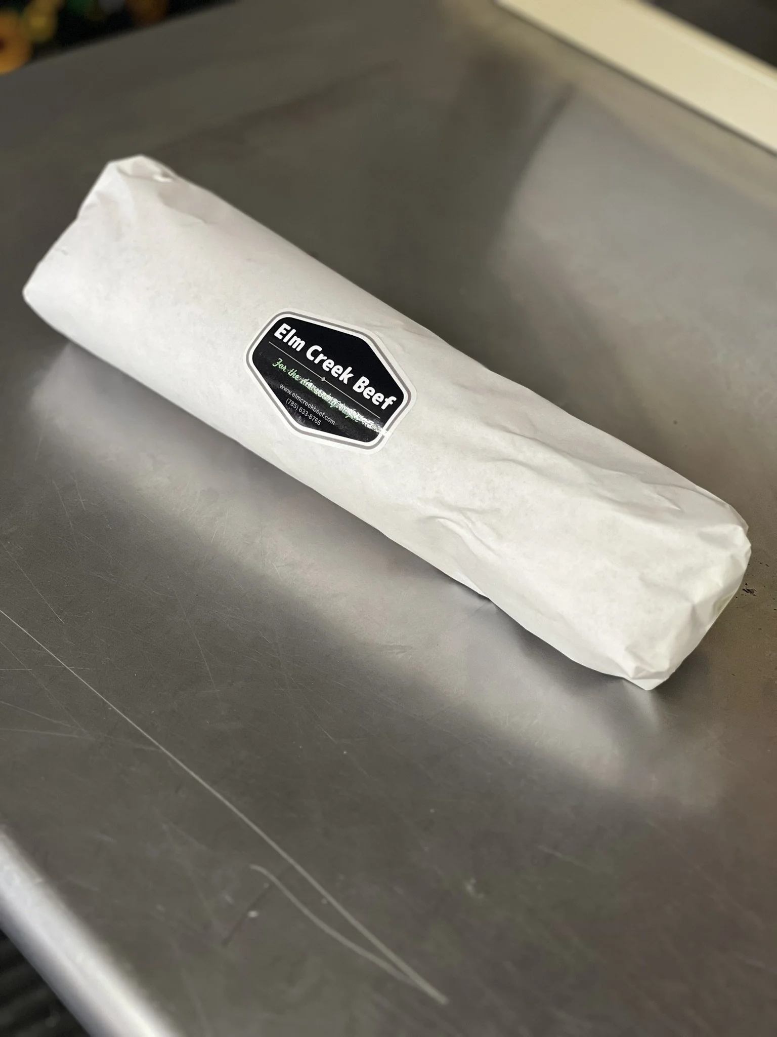 Elm Creek Beef Wrapped sandwich or burrito with a black label that says 'Elm Creek Beer' on a stainless steel surface.