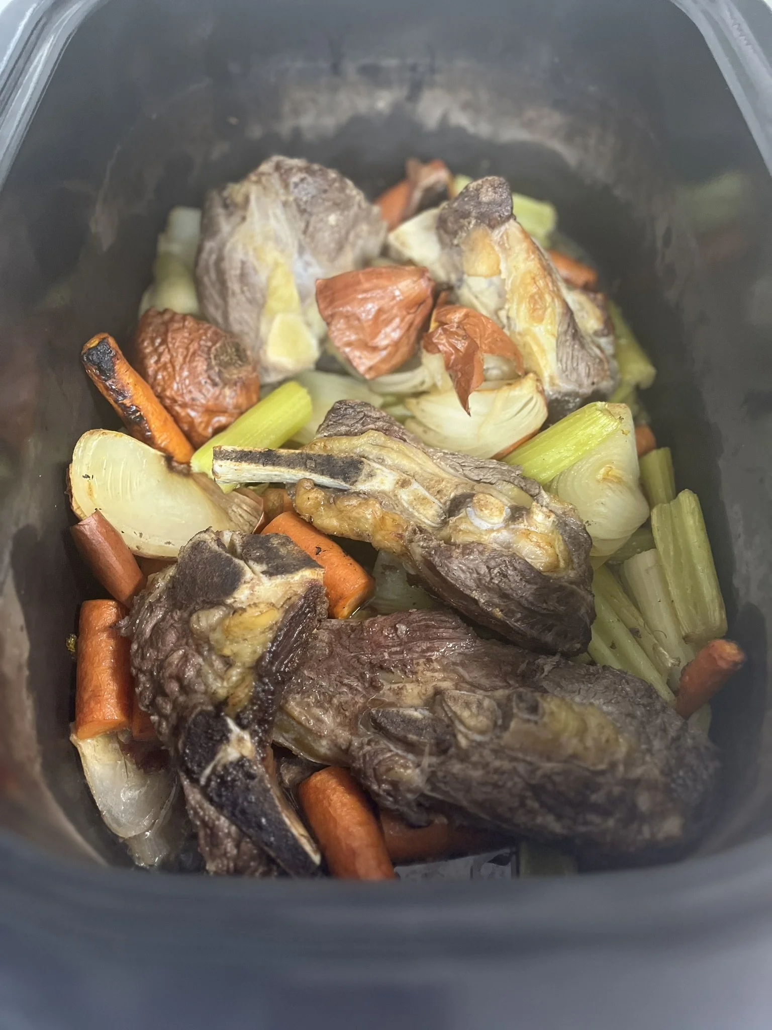 Elm Creek Beef Cooked vegetables including carrots, celery, onions, and meat in a black crockpot.