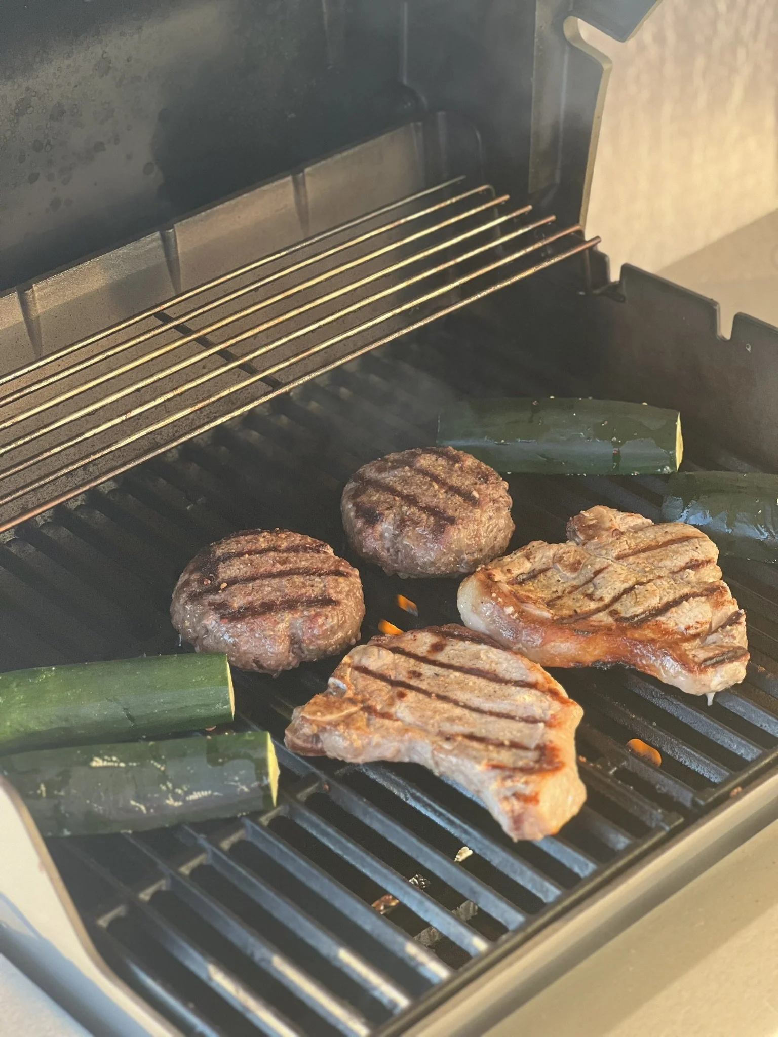 Elm Creek Beef Grilling two hamburger patties and two pork chops in an indoor oven grill, with zucchini pieces on the side.