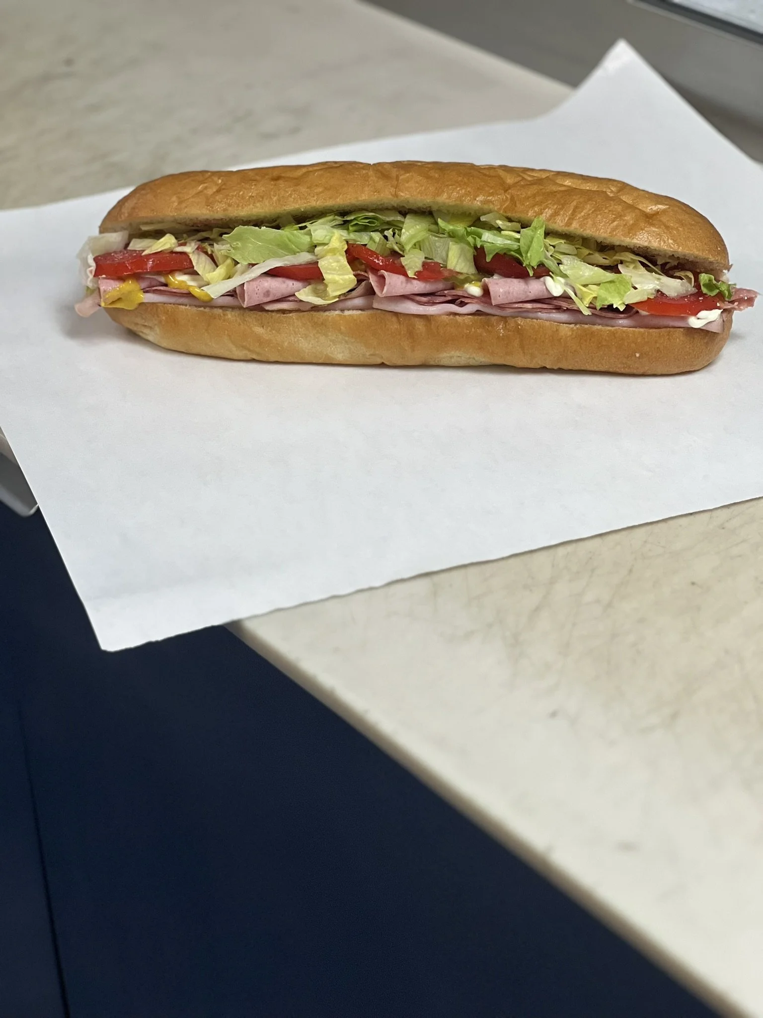 Elm Creek Beef Sub sandwich bread with lettuce, tomato, sliced deli meat, and condiments on white paper