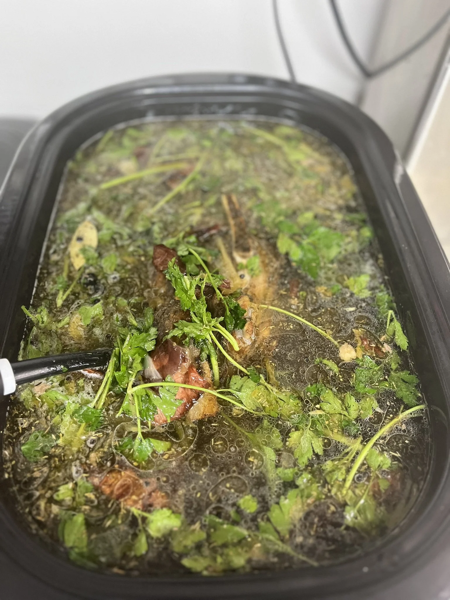 Elm Creek Beef A slow cooker filled with a broth containing herbs, vegetables, and pieces of meat.