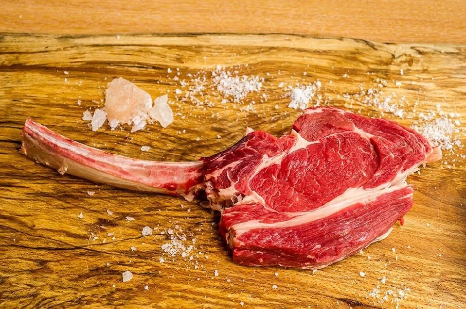 Elm Creek Beef Raw cut of lamb chop on wooden cutting board with salt crystals scattered around.