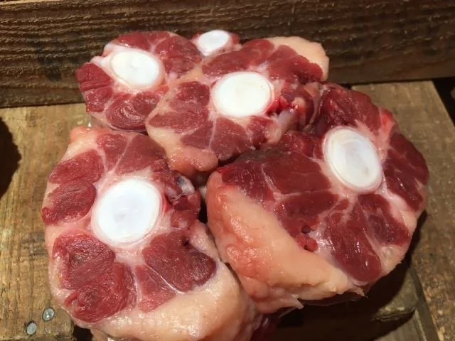 Elm Creek Beef Four cross-cut slices of oxtail beef with bones in a rustic setting on a wooden surface.