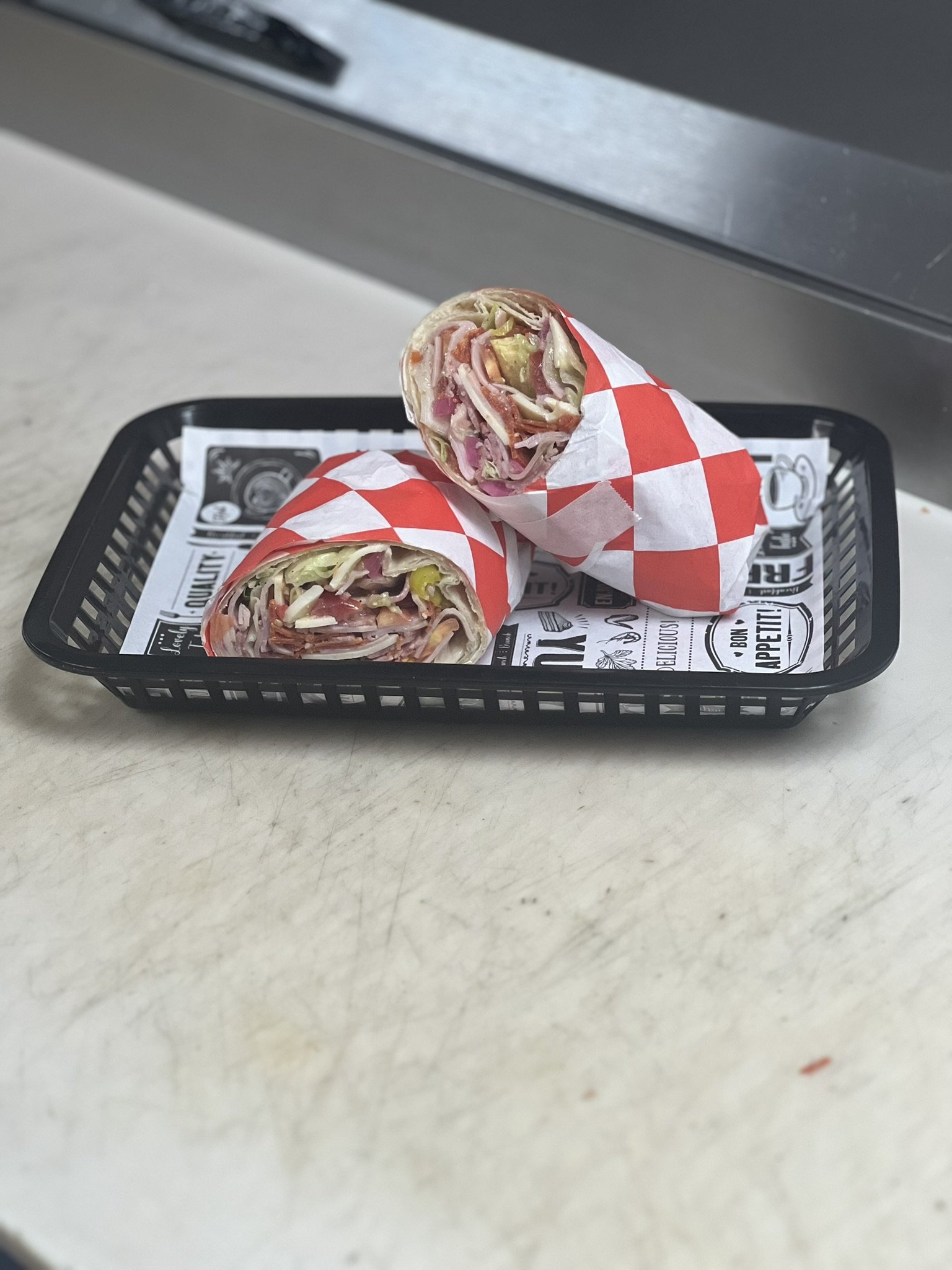 Elm Creek Beef Two wraps with meat, vegetables, and cheese, partially unwrapped on a black tray with printed paper, placed on a beige countertop.
