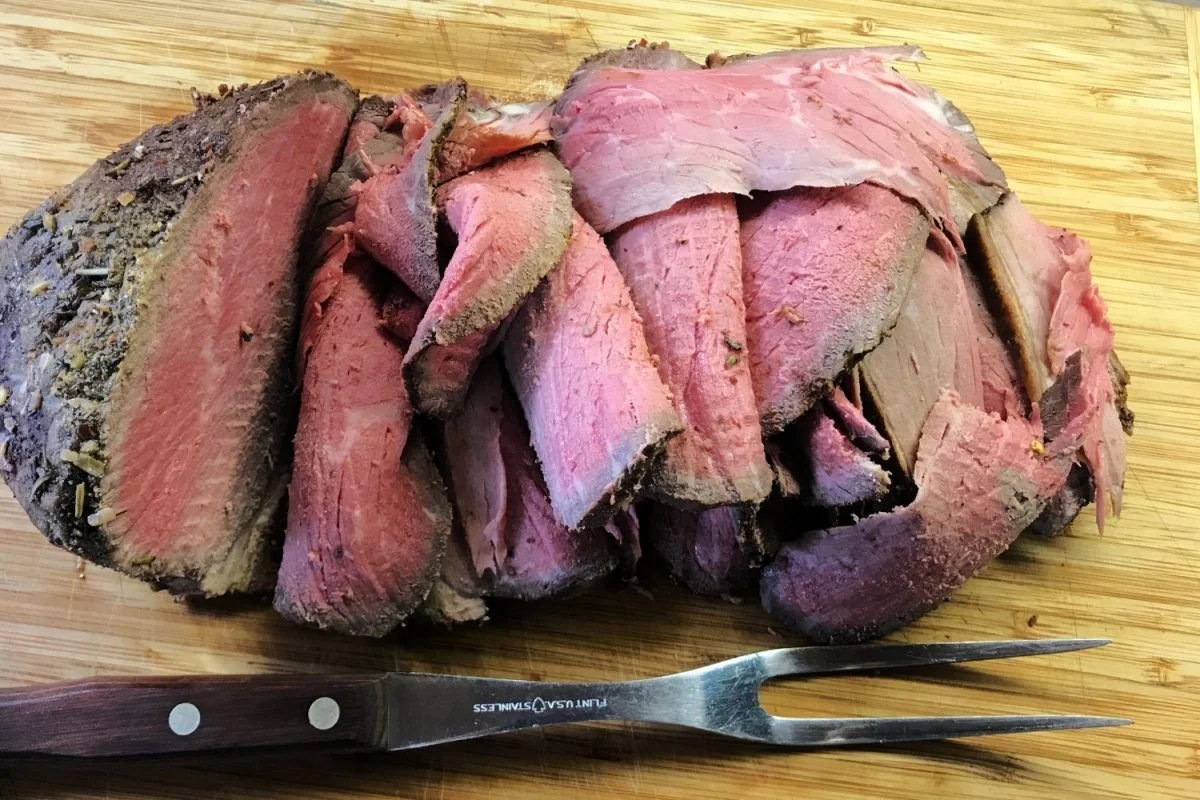 Elm Creek Beef Slices of cooked roast beef on a wooden cutting board with a carving fork.