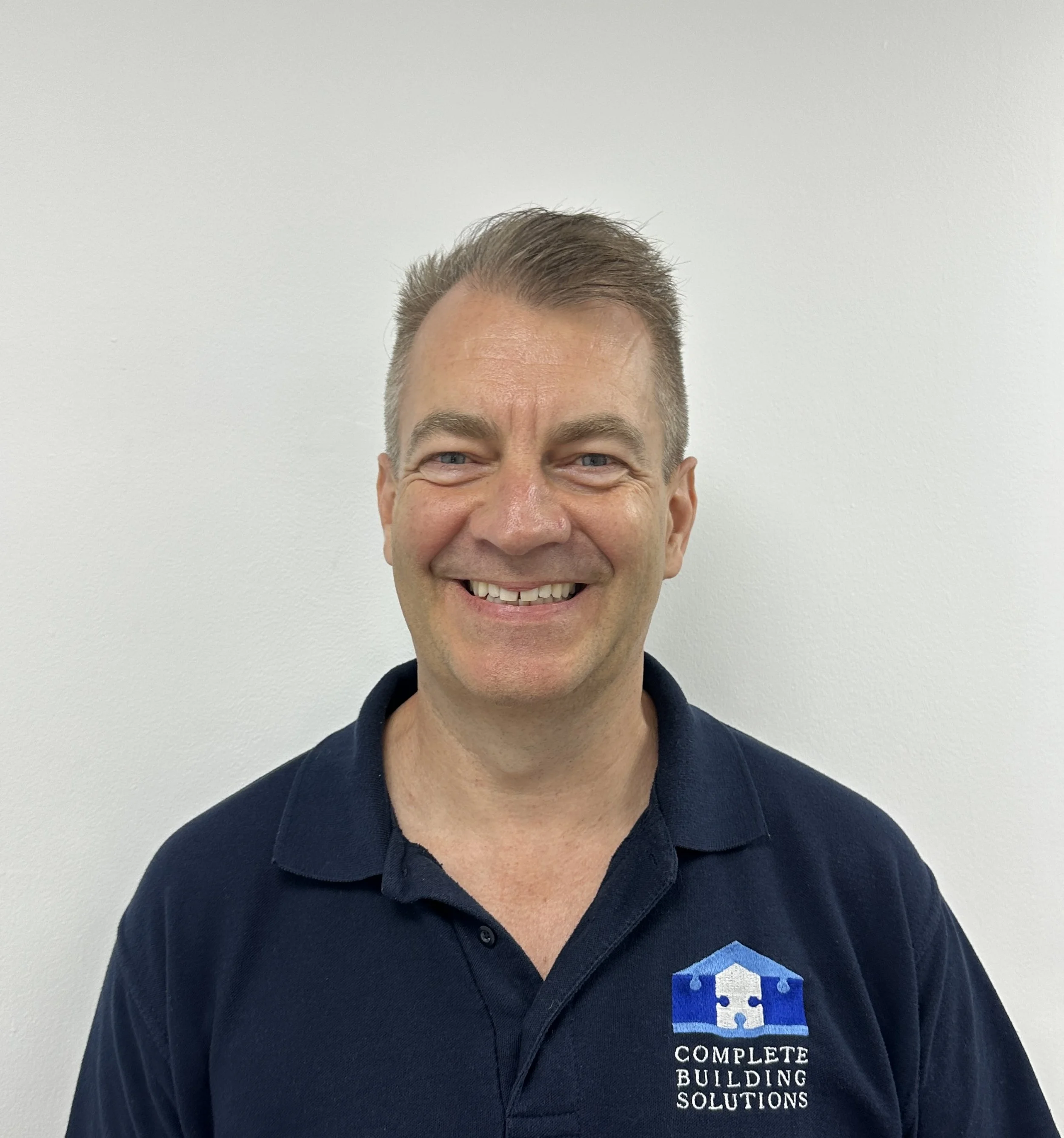 Phil West wearing a navy hoodie with a logo that says 'Complete Building Solutions' stands outdoors on a grassy field with trees in the background.
