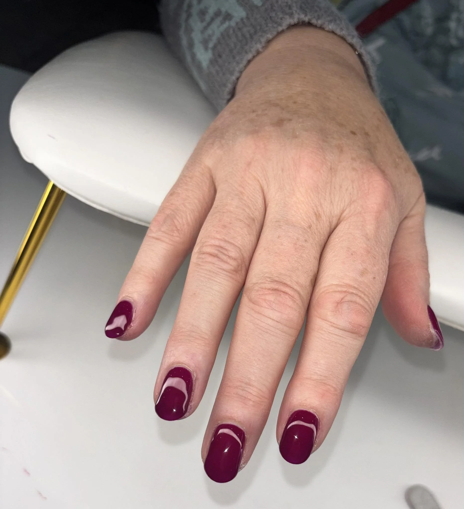 A woman's hand with dark red nail polish resting on a white surface.