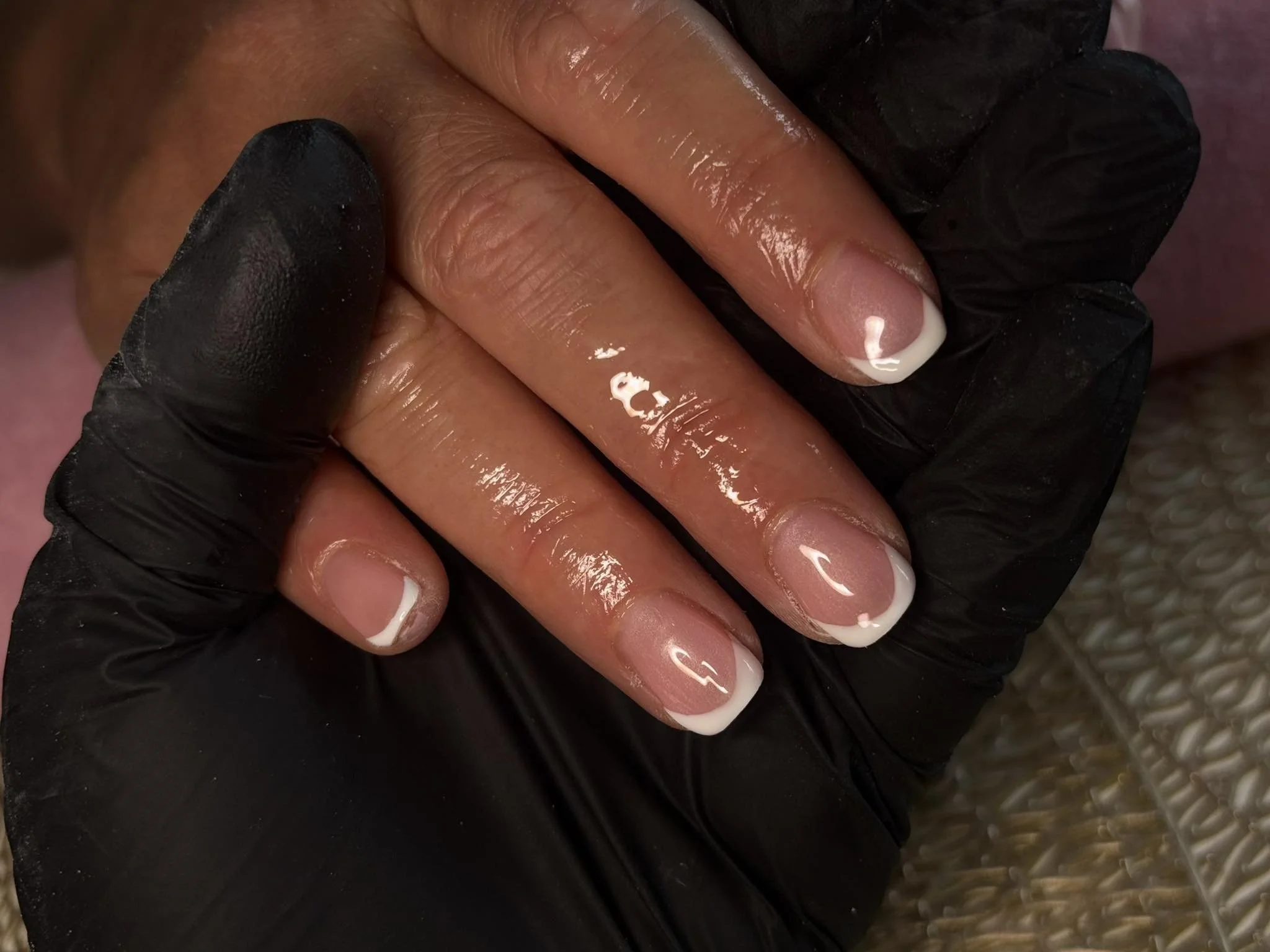 Close-up of a person's nails with French manicure, being treated or painted, with a gloved hand applying or holding the nails.