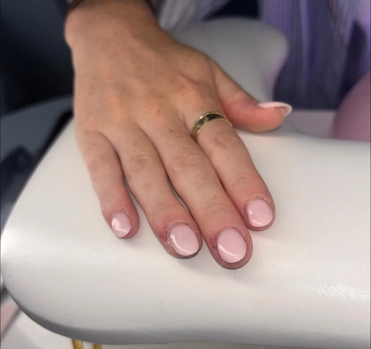 Hand resting on a white surface with freshly manicured nails and a gold ring on the ring finger.