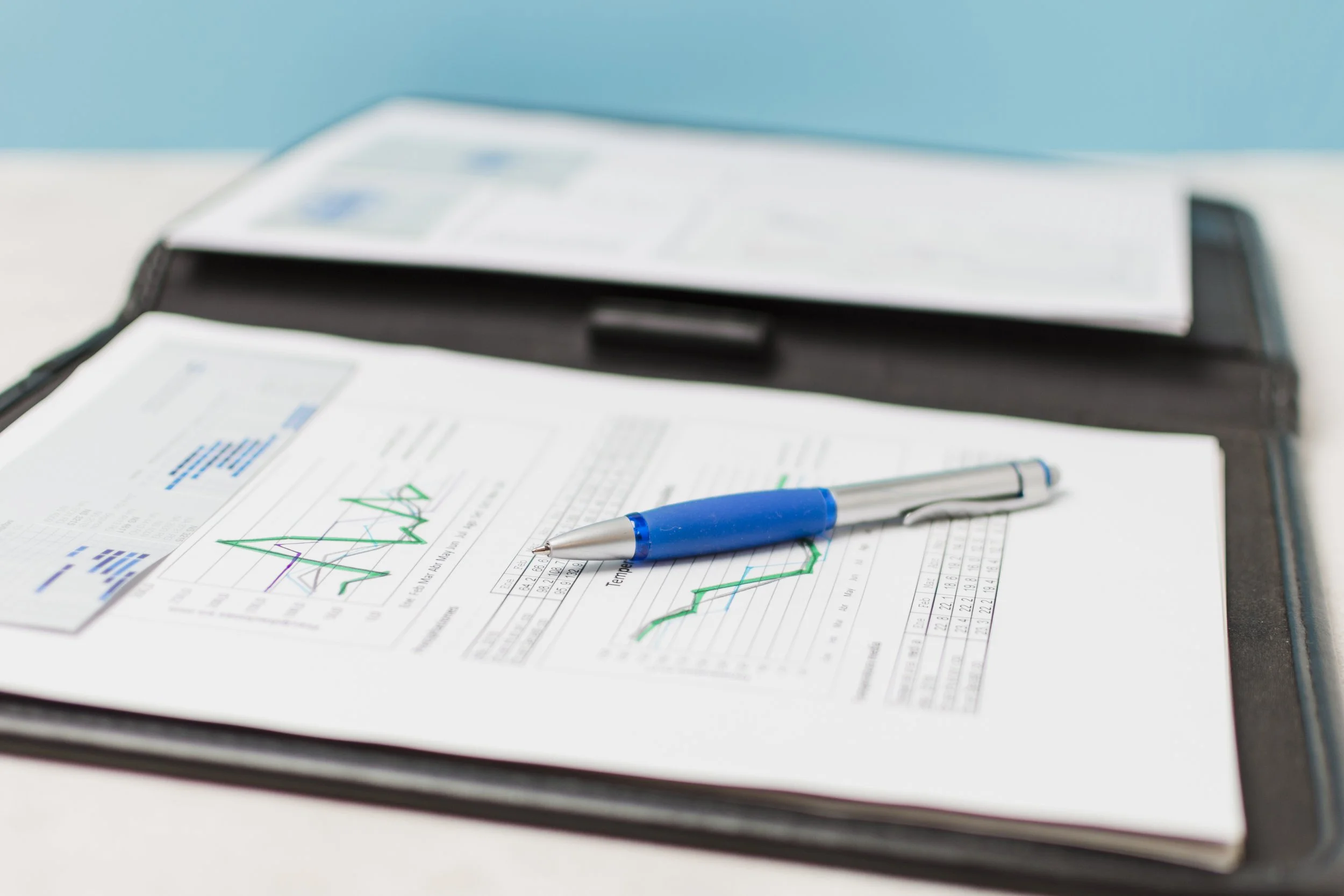 Financial documents with graphs, a blue pen, and a clipboard on a desk.