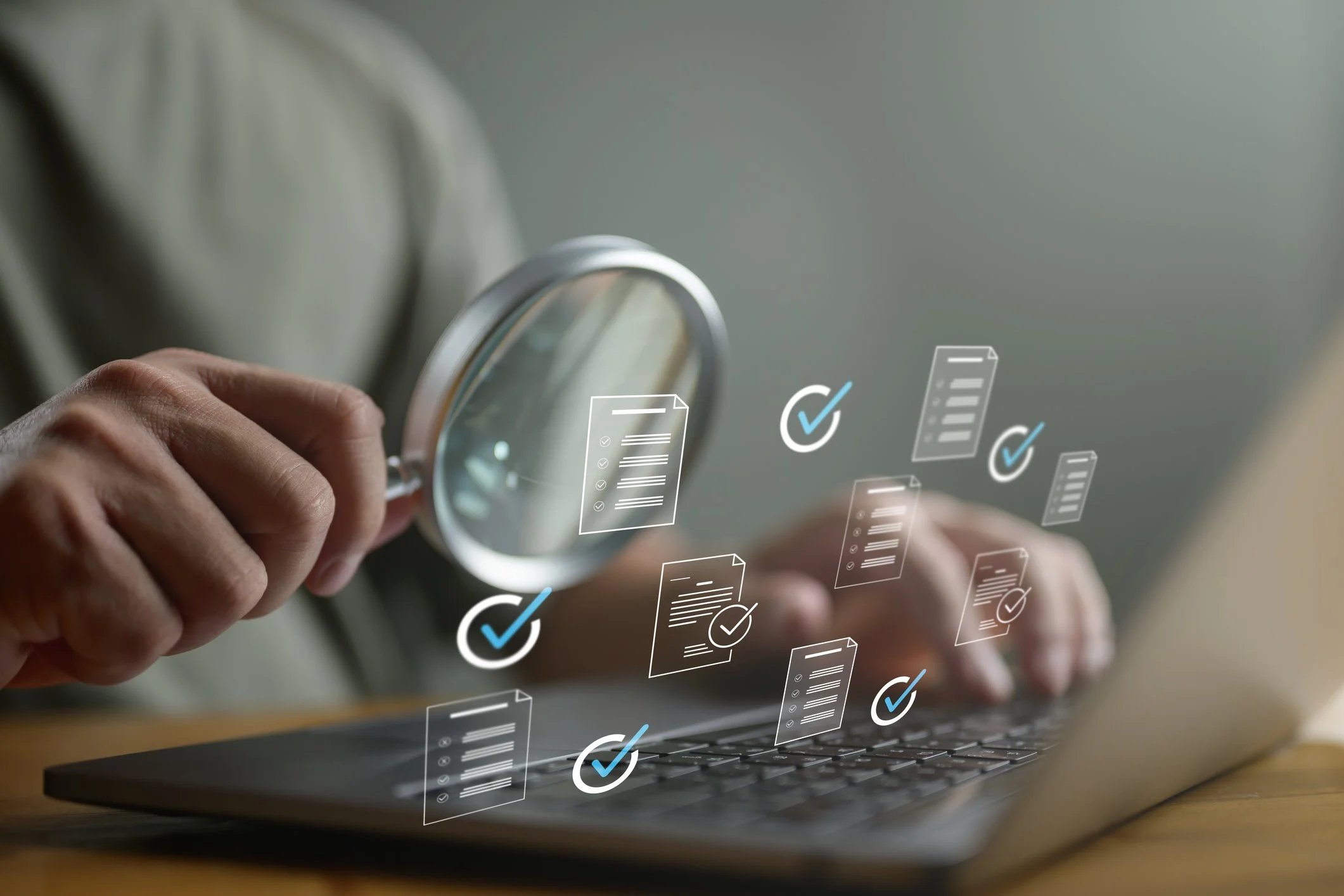 A person holding a magnifying glass over a computer keyboard with digital icons of documents, checkmarks, and checklists appearing above the keyboard.