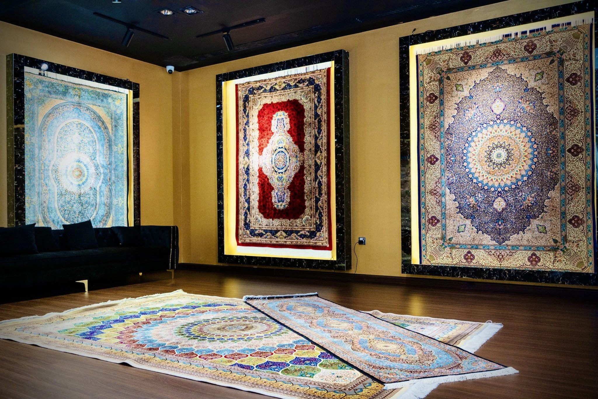 Display of three large, traditional Silk Carpets with intricate patterns and vibrant colors in an art gallery.