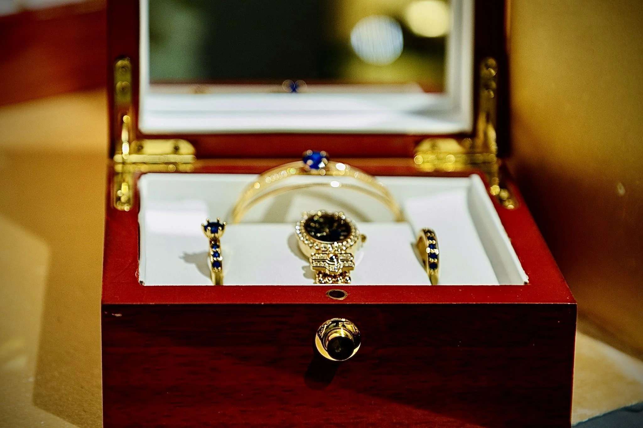 A jewelry box with a mirror on top, containing gold jewelry with blue stones, inside a red case.