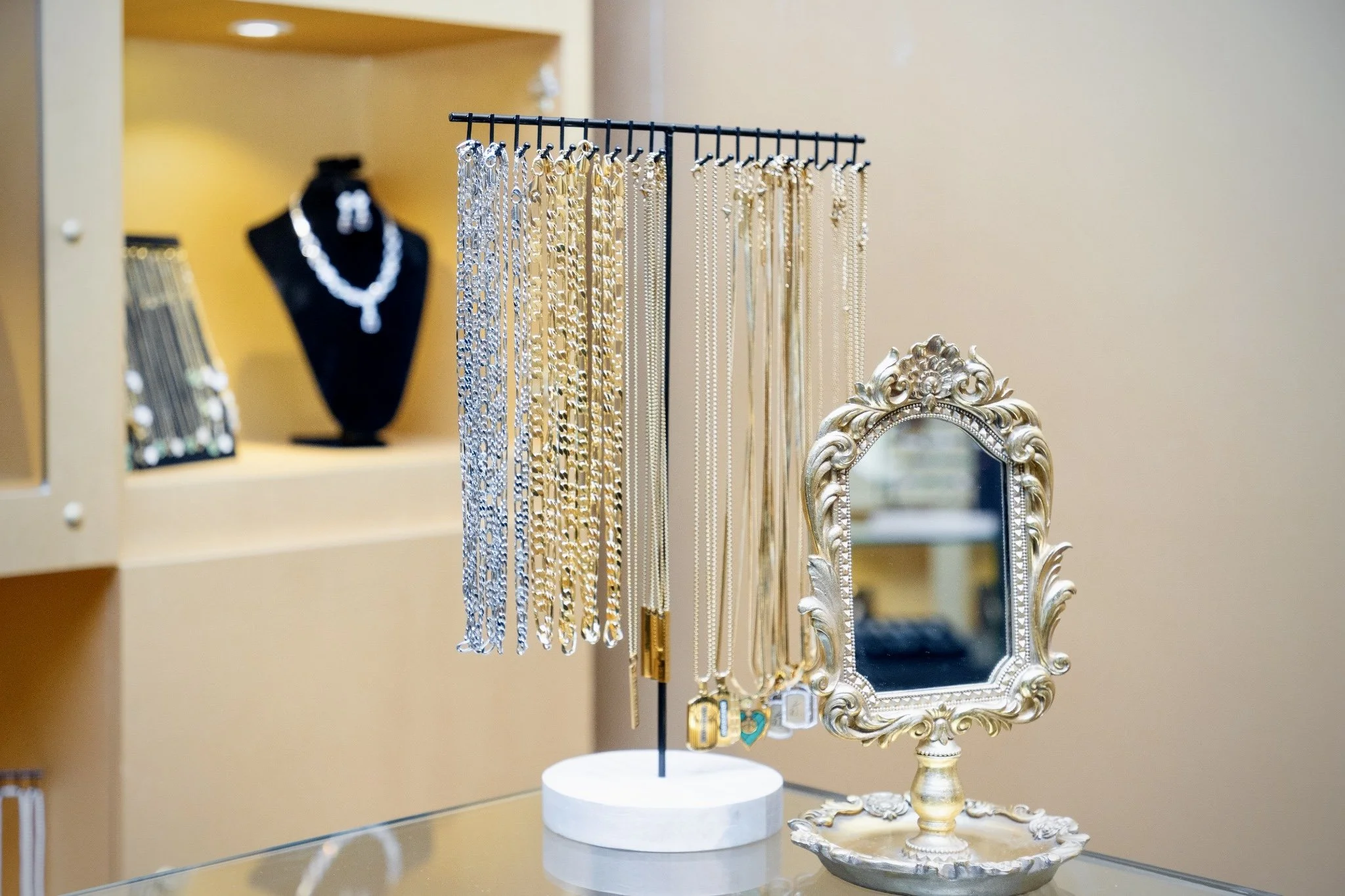 Jewelry display with necklaces and earrings on a stand, mirror, and jewelry pieces on a decorative tray.