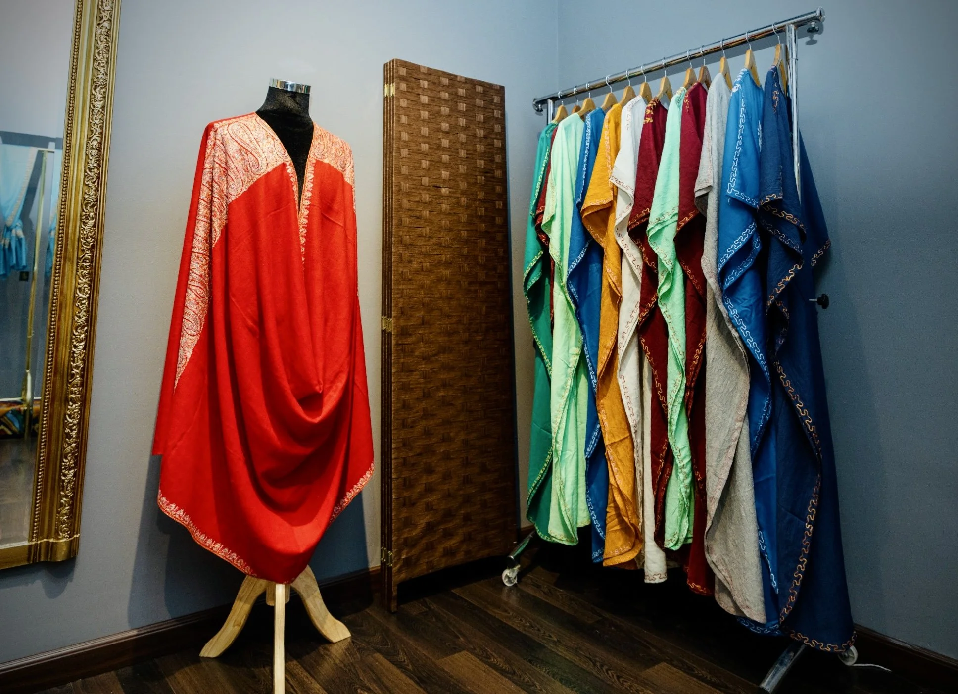 Display of colorful traditional dresses on a clothing rack and a red dress on a mannequin in a boutique fitting room.