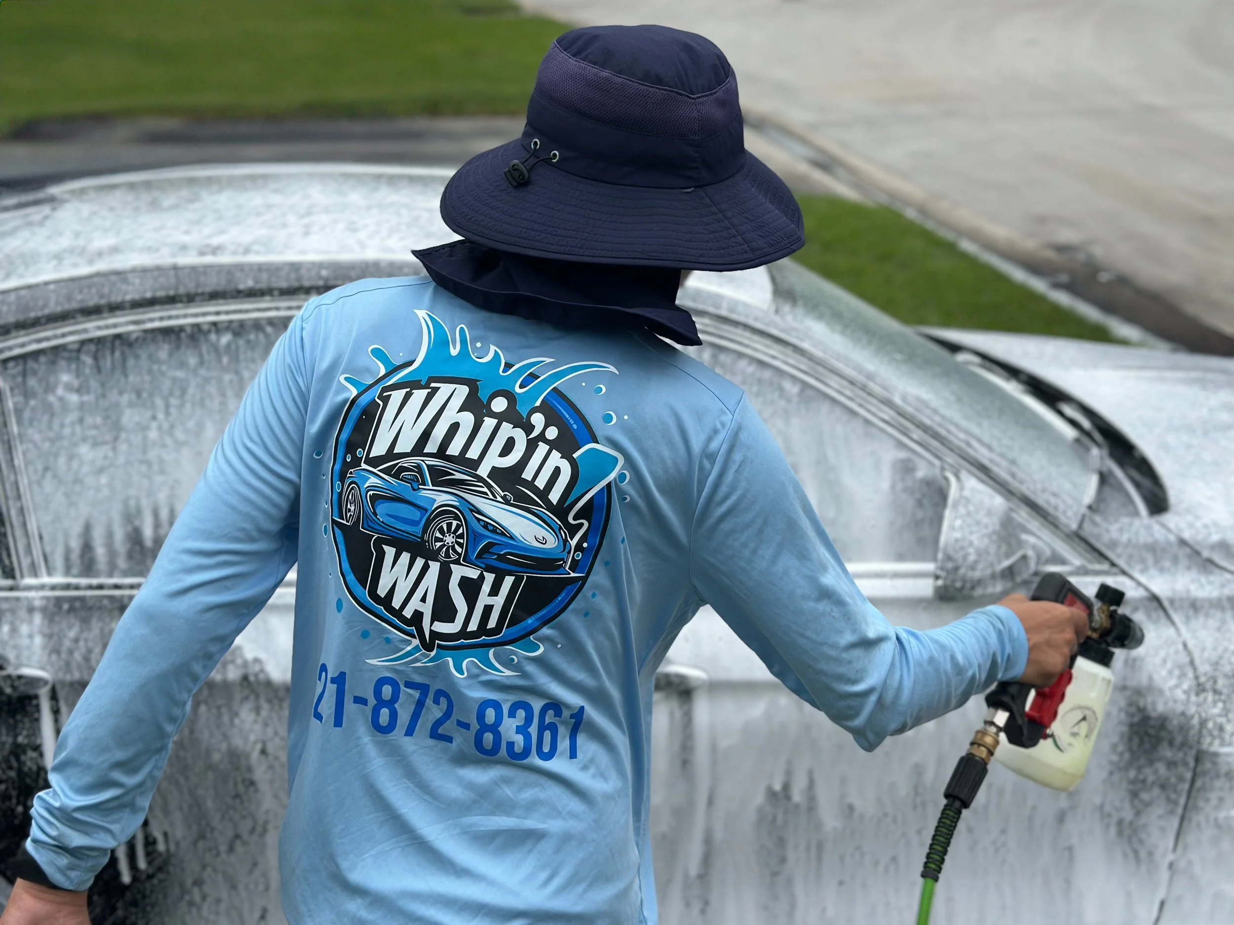 DeVon wearing a dark blue wide-brimmed hat and a light blue shirt with a logo of a car and the words Whip'in Wash on the back, Detailing a Bmw M3.
