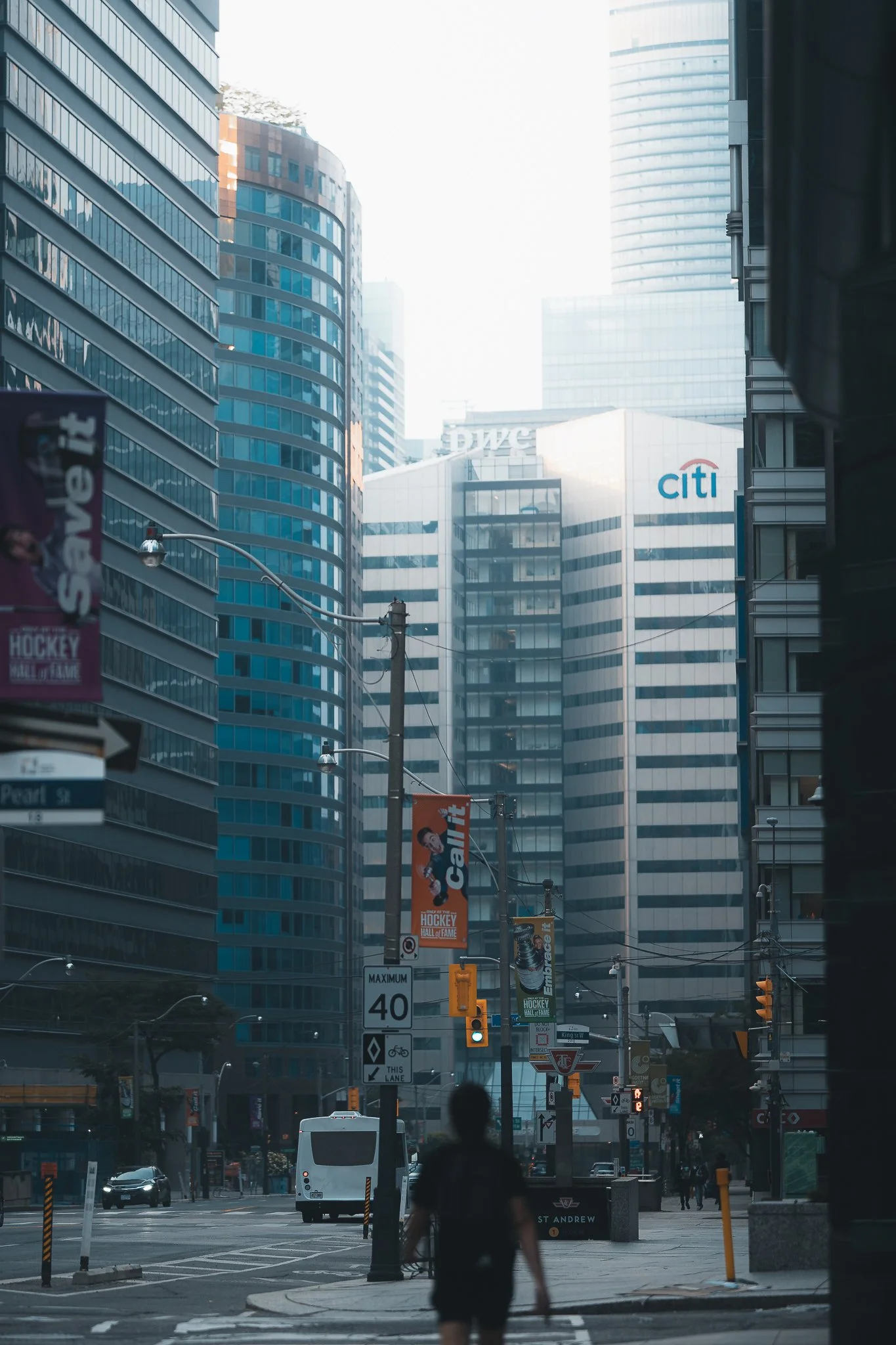 City street scene with tall glass buildings, a person walking, traffic lights, and signs, including a Citi bank sign and hockey banners.