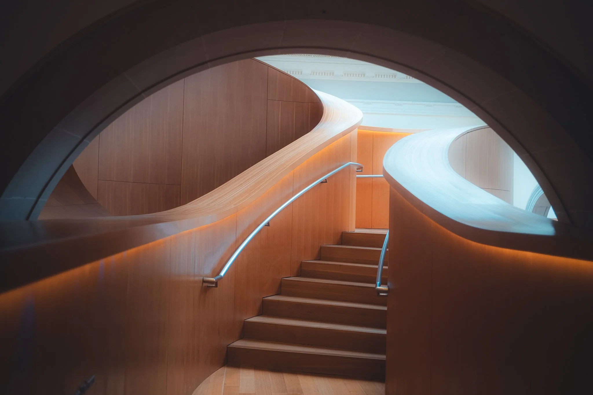 Curved wooden staircase with metal handrails inside a modern building.