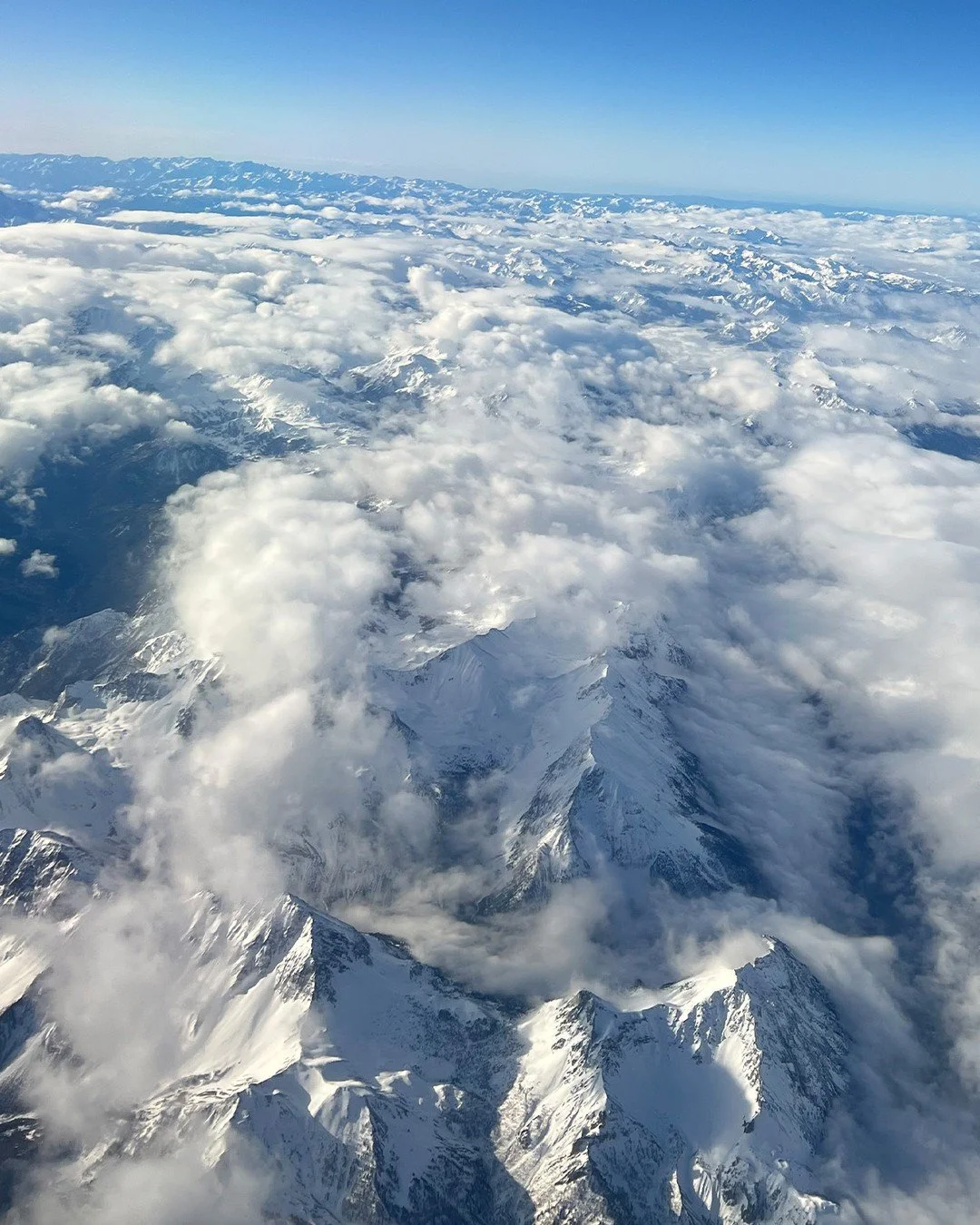 Flying over the Alps en route to Milan&mdash;snow-covered peaks, drifting clouds, and a reminder of how closely our work is tied to place. A spectacular view before touching down in Italy.