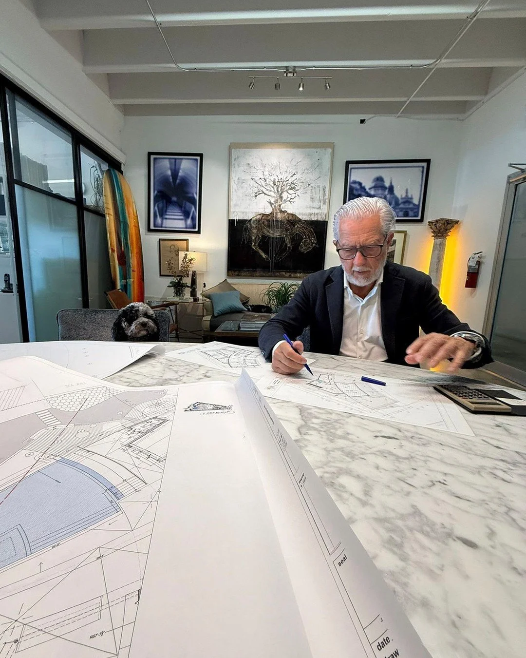 The plans are spread across marble. The irony isn't lost on us.

This is where the work actually happens &mdash; before the installation, before the finished room, before the photograph. Sandro sits down with the drawings and figures out exactly how 