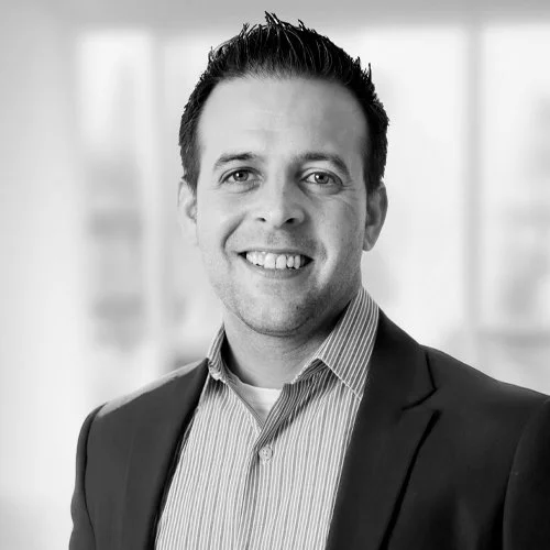 Black and white photo of a smiling man wearing a striped dress shirt against a plain background.