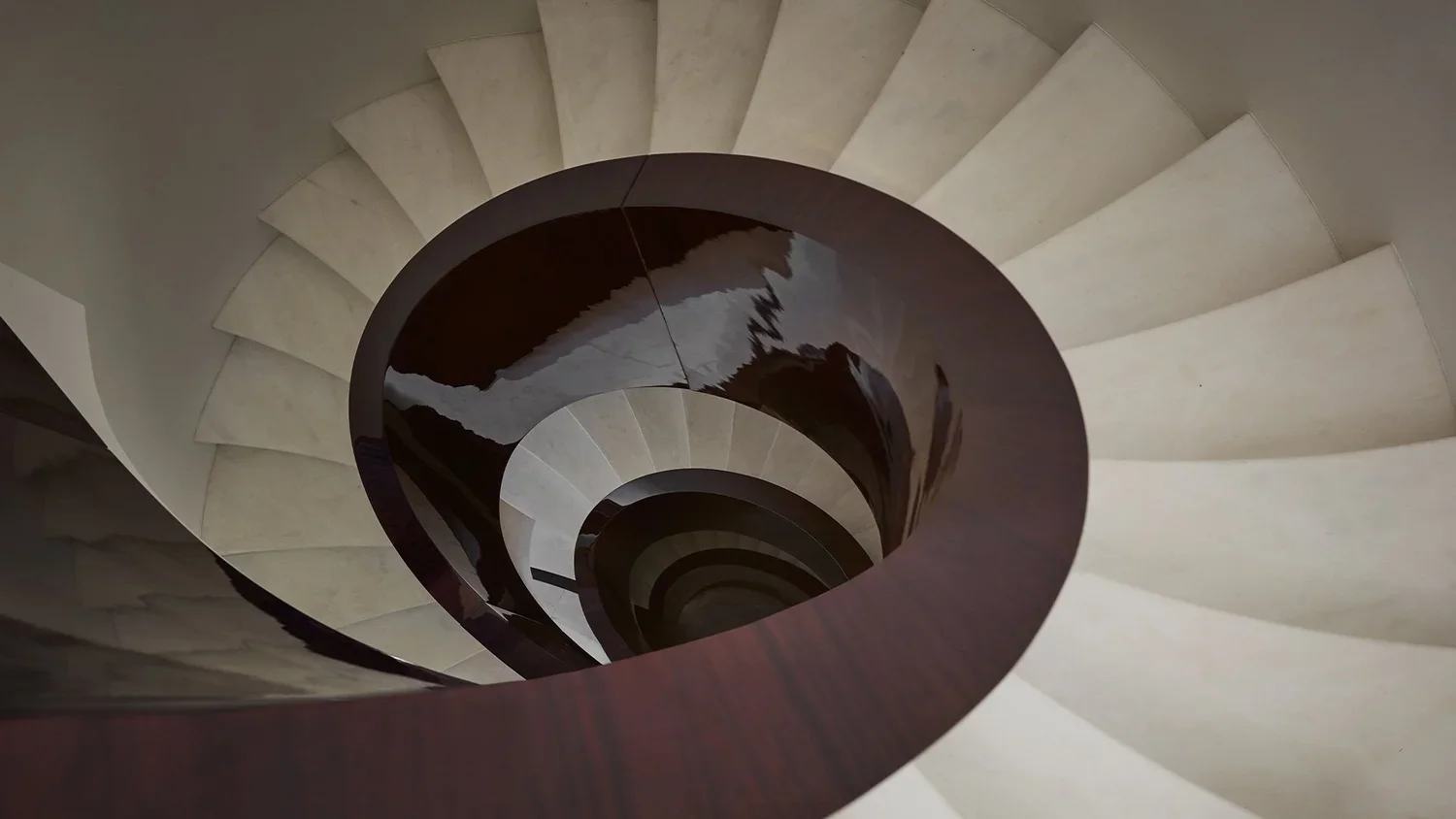 Looking down an indoor spiral staircase with white steps and a dark rim, creating a swirl pattern.