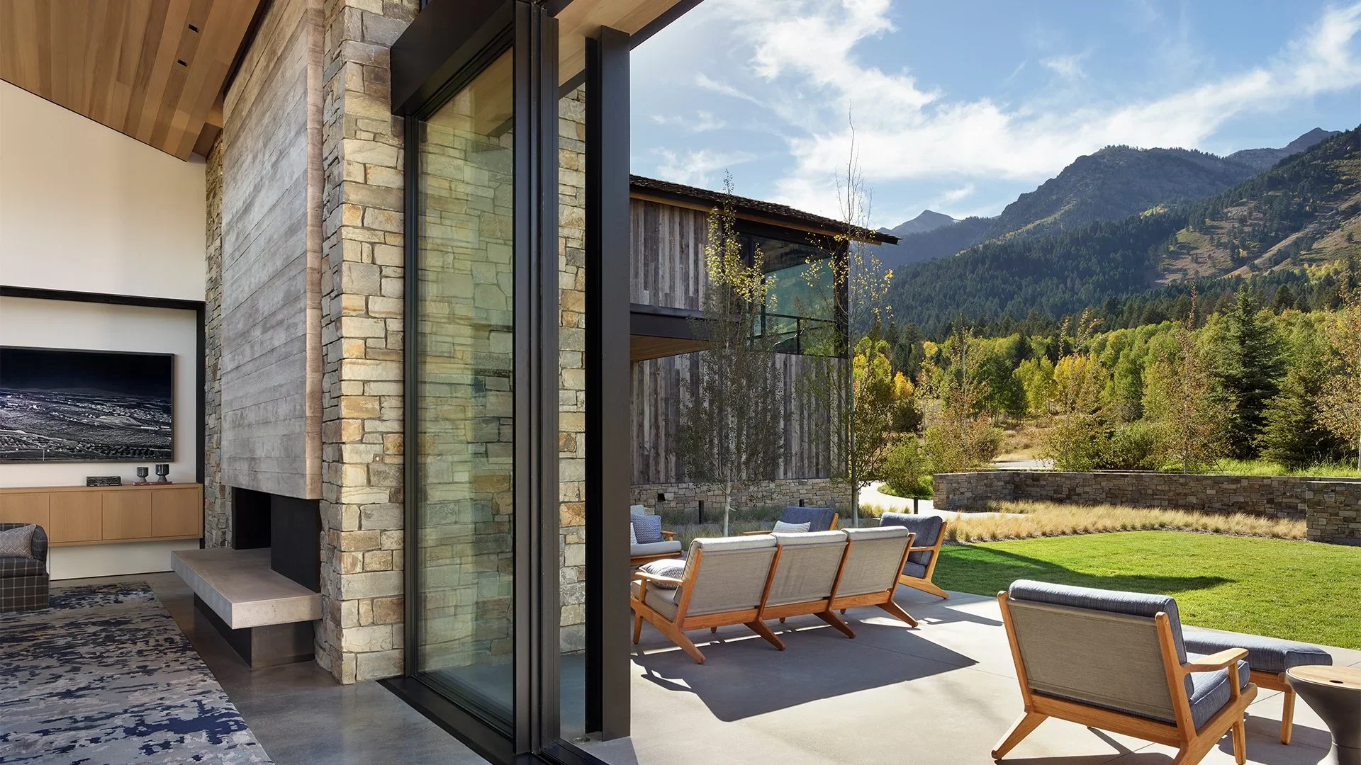 Modern house interior with sliding glass doors leading to a patio, overlooking a landscape with green grass, trees, and mountains.