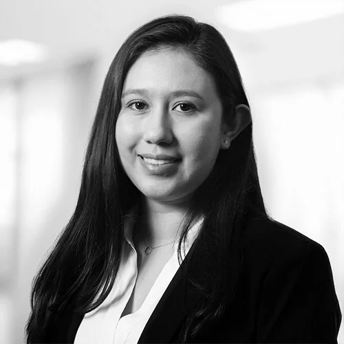 Black and white portrait of a young woman with long dark hair, wearing a blazer and a white shirt, smiling slightly.