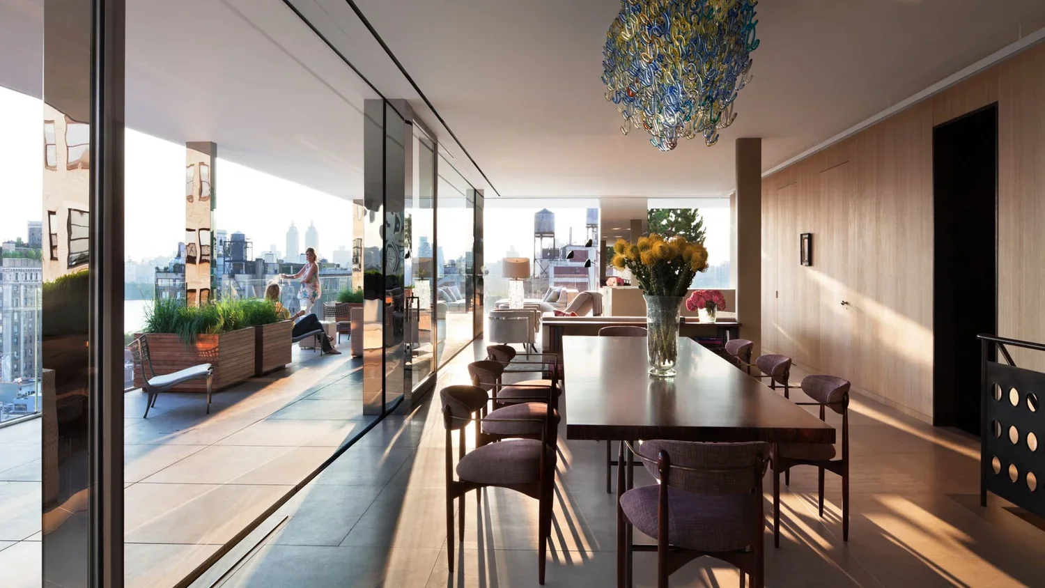Modern apartment with dining area, city skyline view, outdoor balcony with seating, and interior decor including flowers and artwork