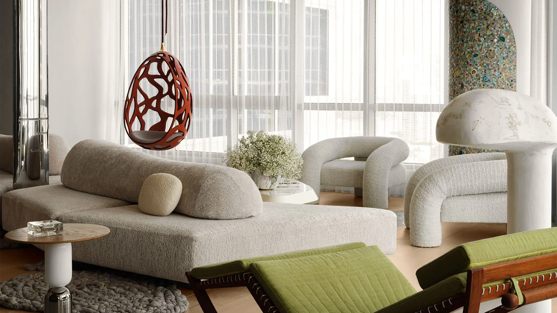 Modern living room with white textured furniture, a hanging red decorative basket, a mushroom-shaped lamp, green lounge chairs, a white round coffee table with flowers, and large windows with sheer curtains.