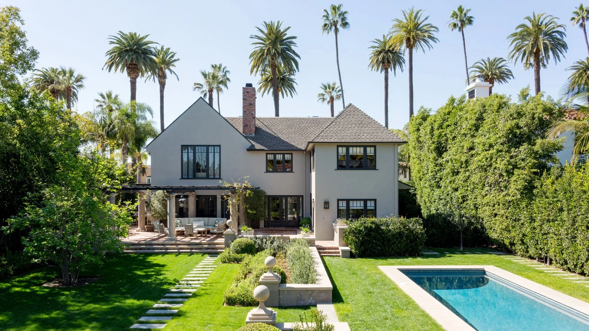 Large modern house with a backyard, palm trees, a swimming pool, and a patio with outdoor furniture.