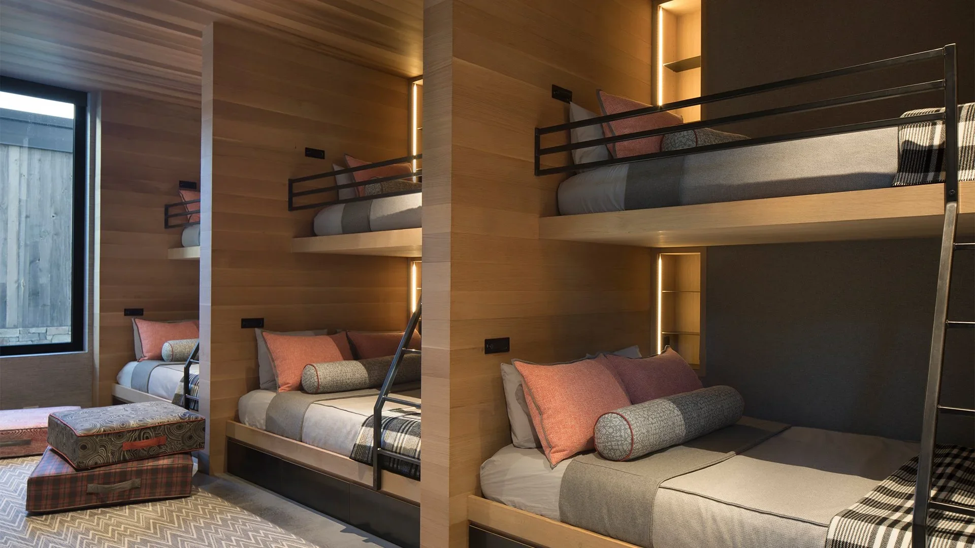 Interior of a modern bedroom with two sets of bunk beds, featuring wooden walls, a window, and patterned cushions.