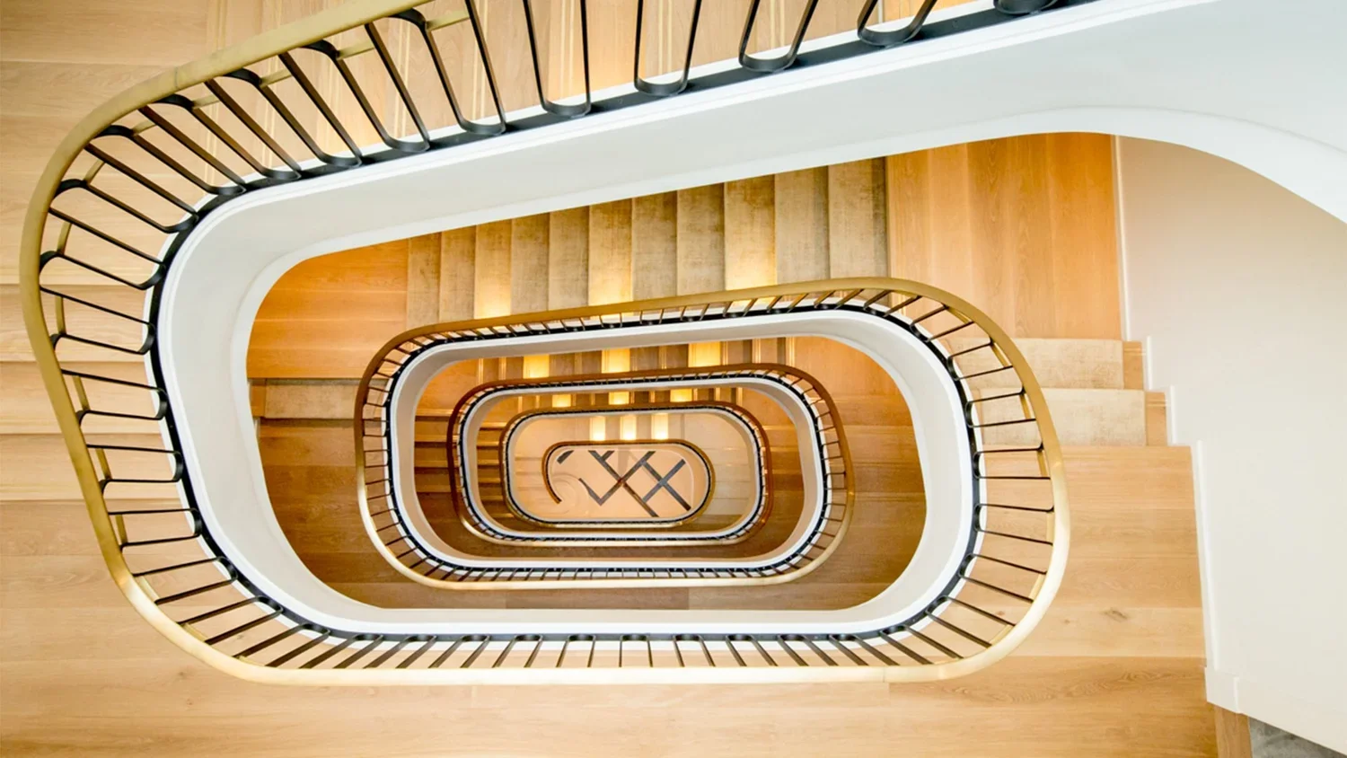 Top-down view of a spiral staircase with wooden steps, white sides, and black metal railing, descending through multiple levels.