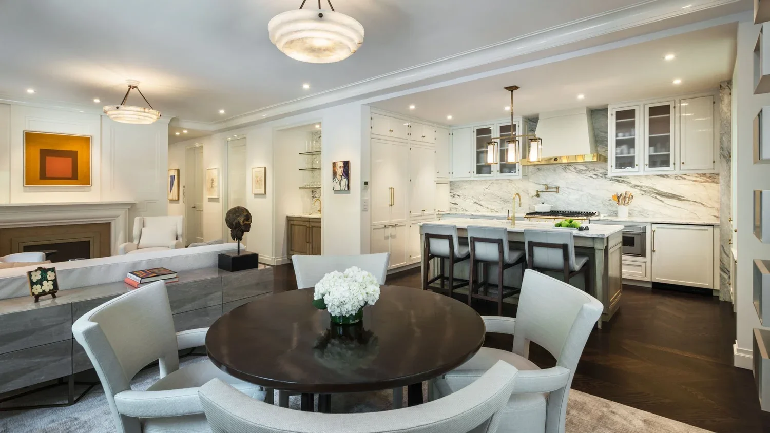 Open-concept kitchen and dining area with white cabinetry, marble backsplash, dark wood floors, and modern lighting fixtures