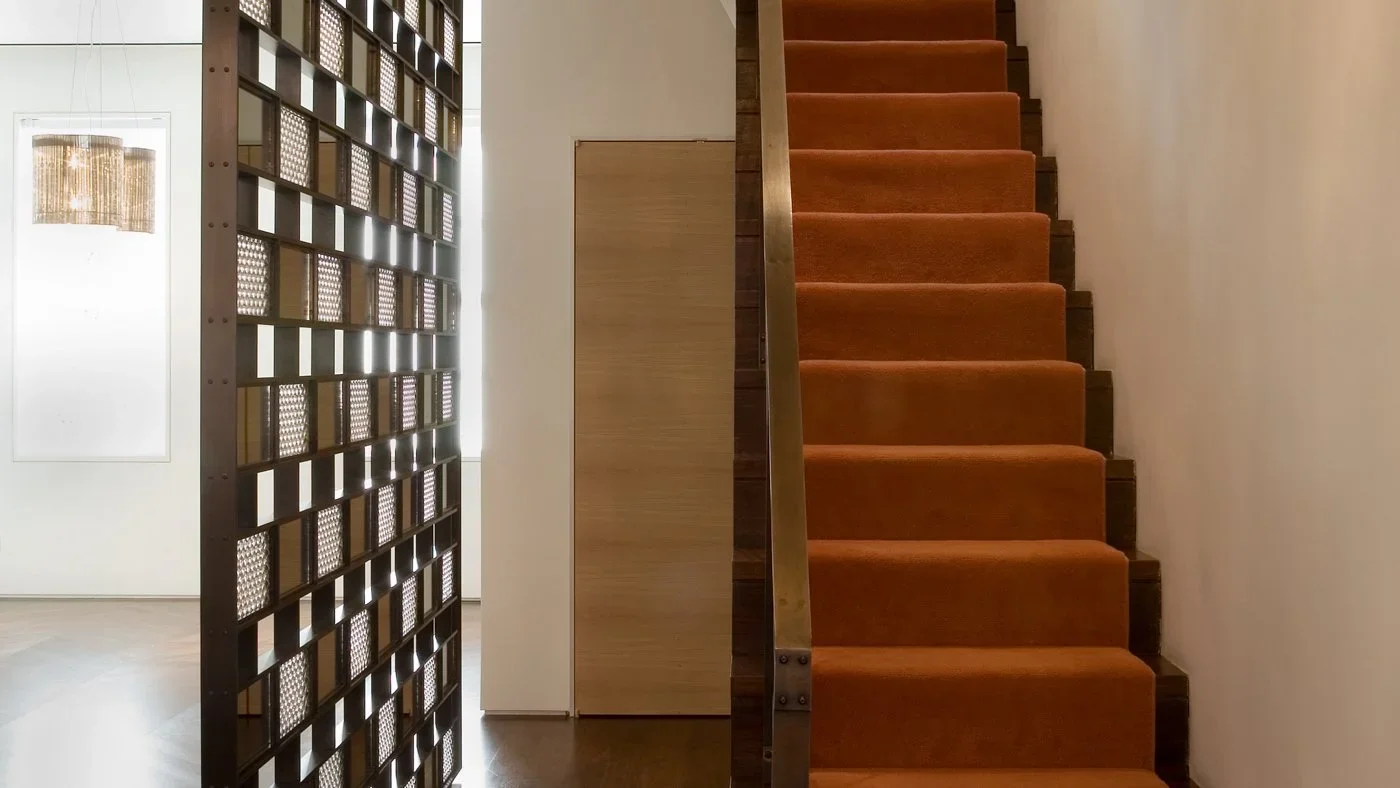 Interior view of a staircase with orange carpeted steps, a wooden railing, and decorative partition in a modern building.