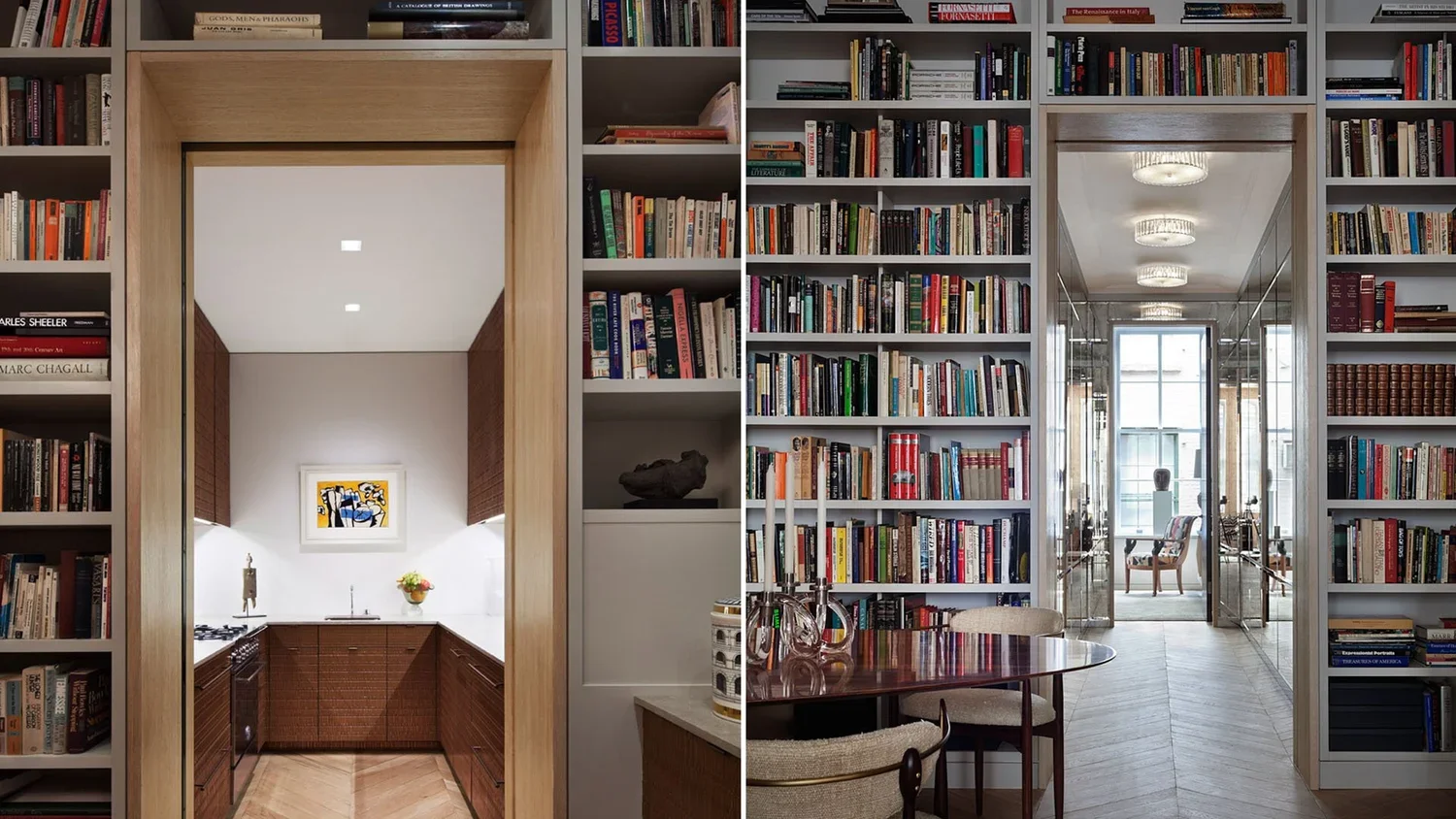Split view of two rooms: on the left, a kitchen with wood cabinets, a white wall, and artwork; on the right, a library with bookshelves, a round table, and a hallway with glass walls and a window.