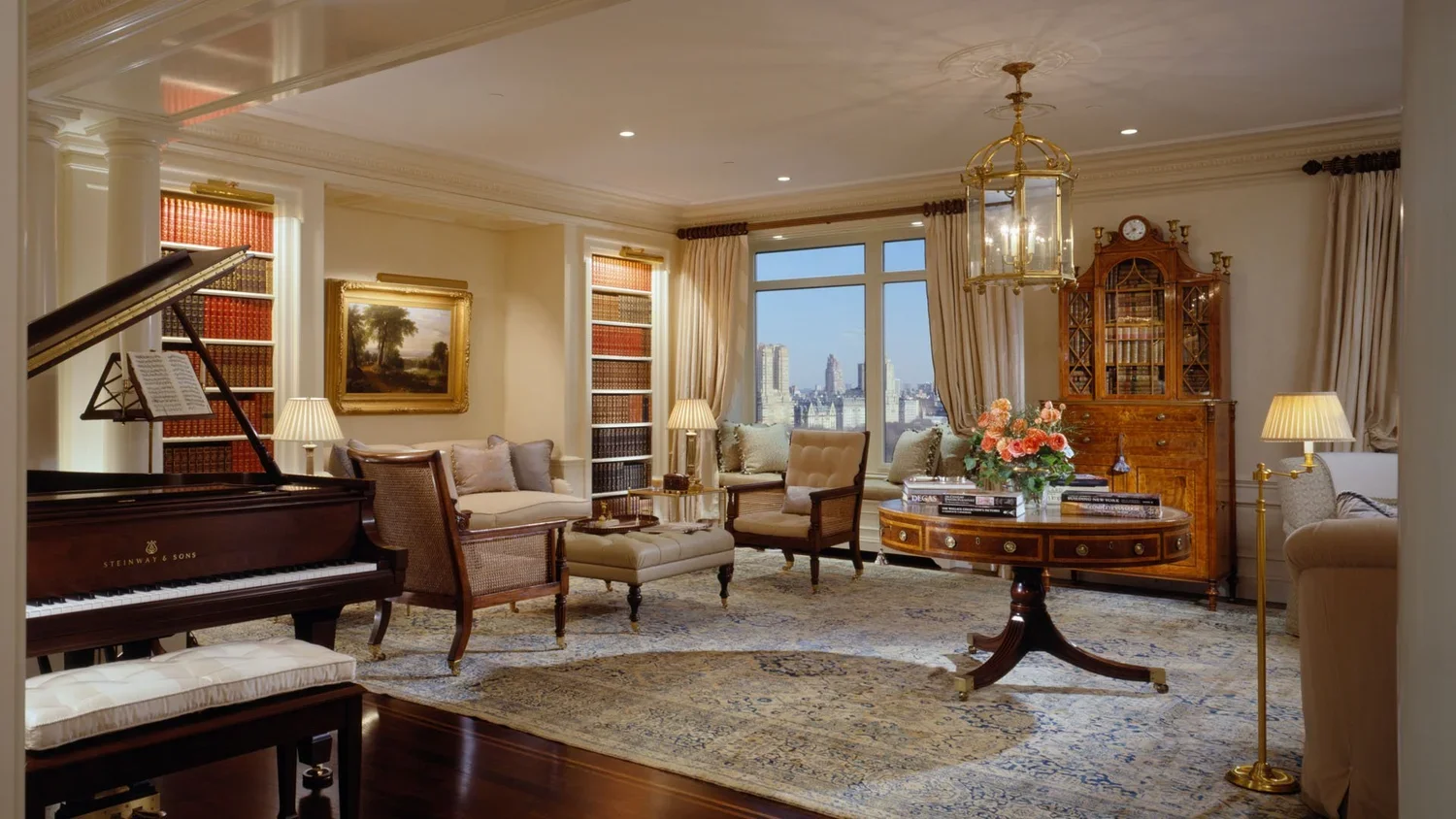 Elegant living room with grand piano, armchairs, sofa, bookshelf, floral arrangement, paintings, and city skyline view through large window.