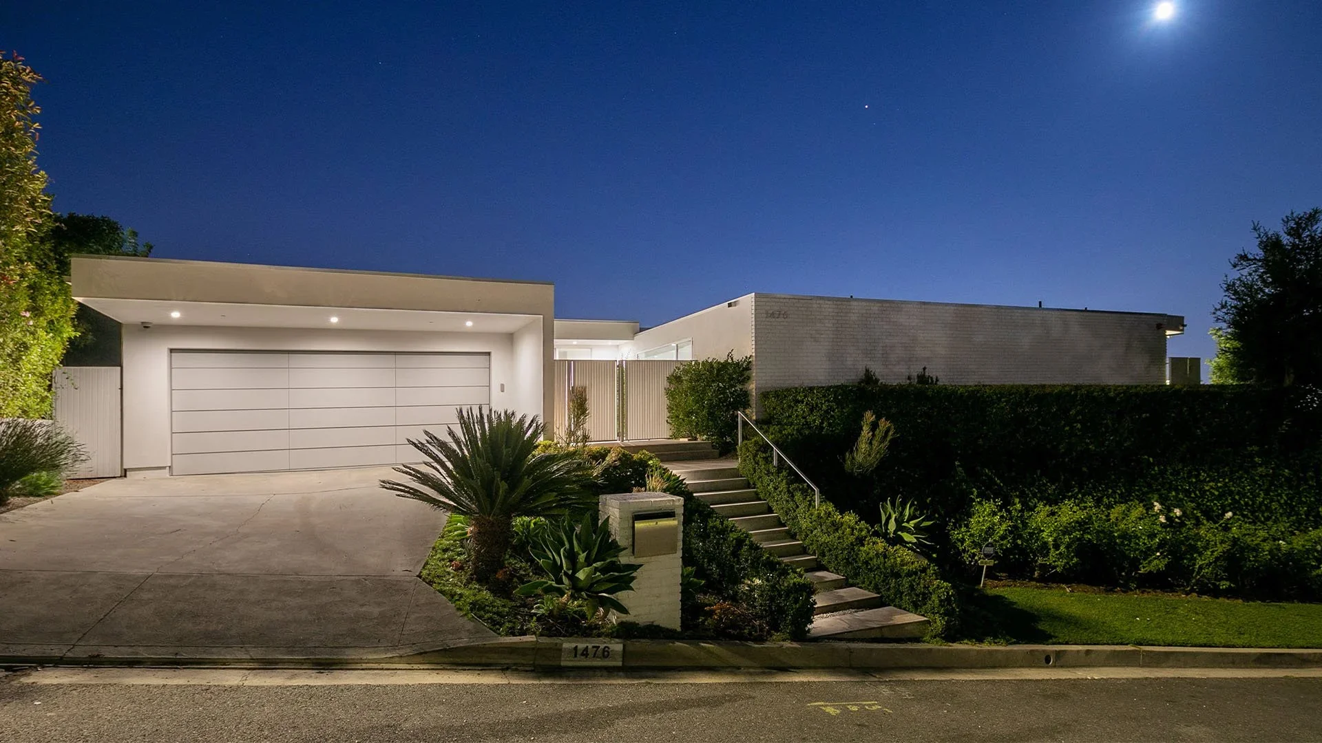 Modern house with white exterior, garage, front steps, and lush landscaping at night under a clear sky.