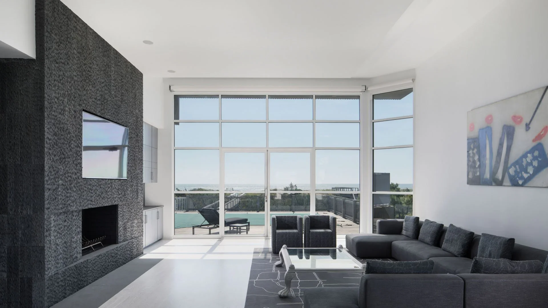 Modern living room with large windows, black sectional sofa, artwork, TV, and outdoor deck view