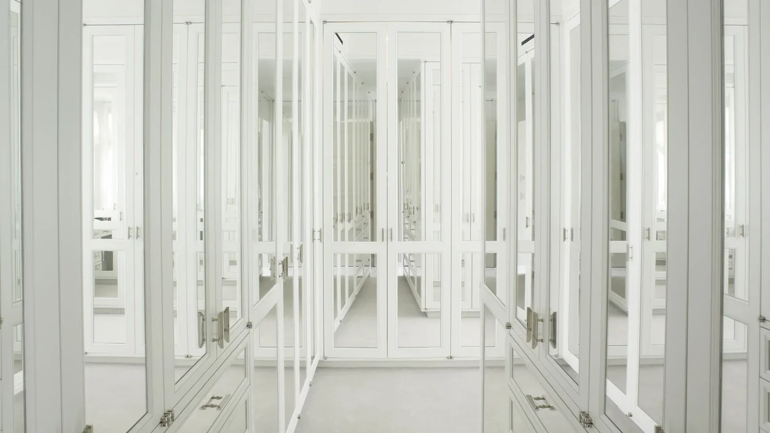 A walk-in closet with white built-in lockers and mirrored doors.