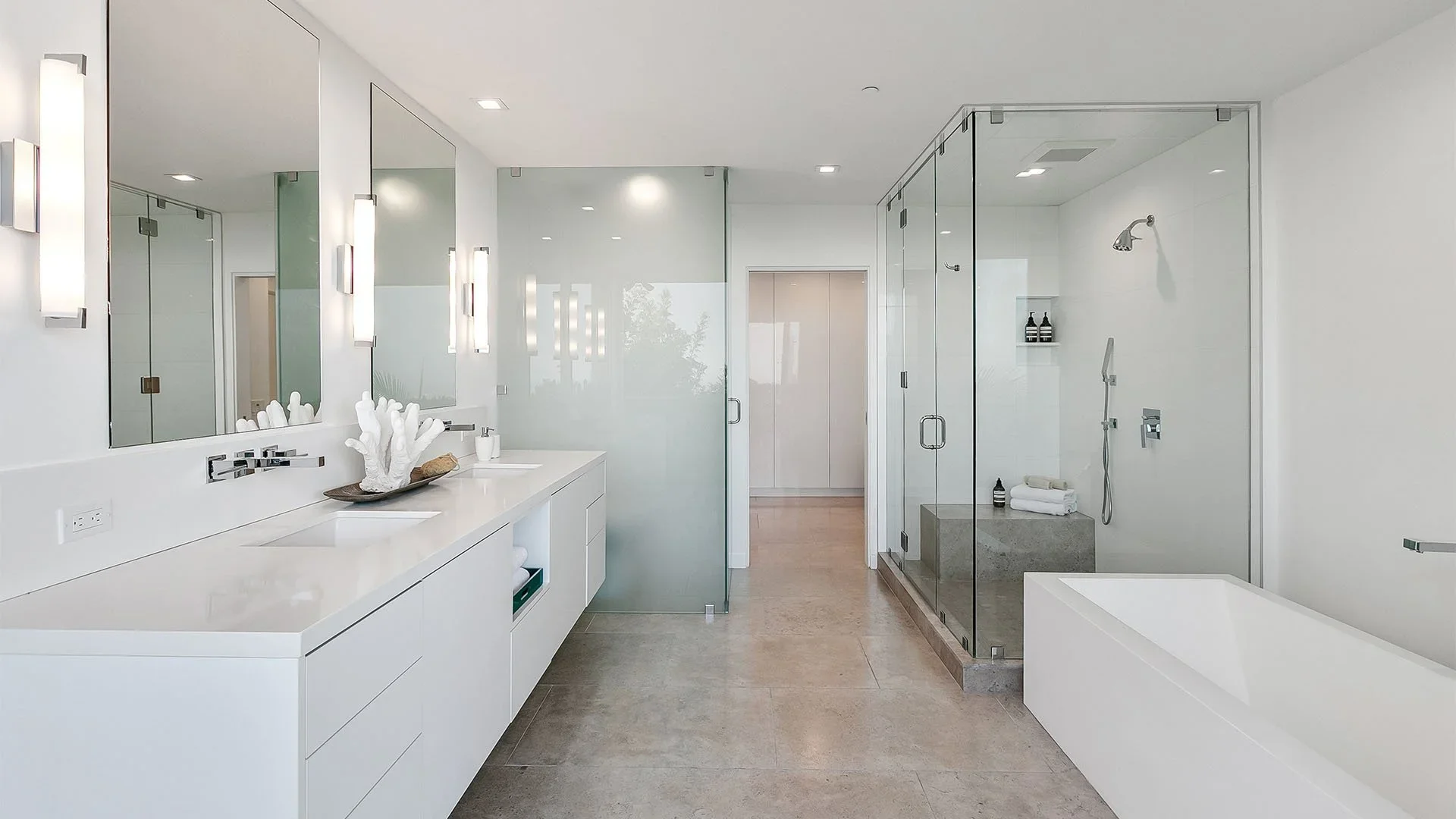 Modern bathroom with double vanity, large mirrors, glass-enclosed shower, and a built-in bathtub, all in a minimalist white and neutral color scheme.