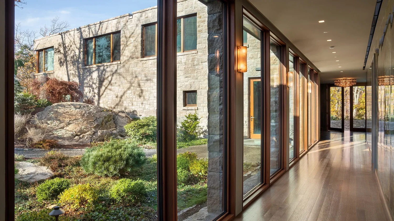 Interior view of a hallway with glass walls showing an outdoor garden with rocks and trees.