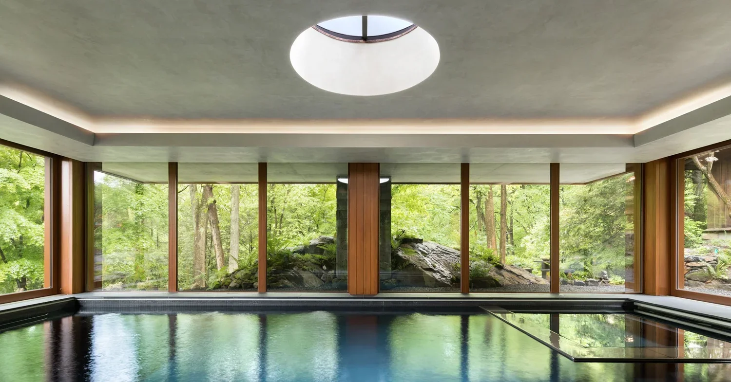 Indoor pool with large windows overlooking a wooded landscape