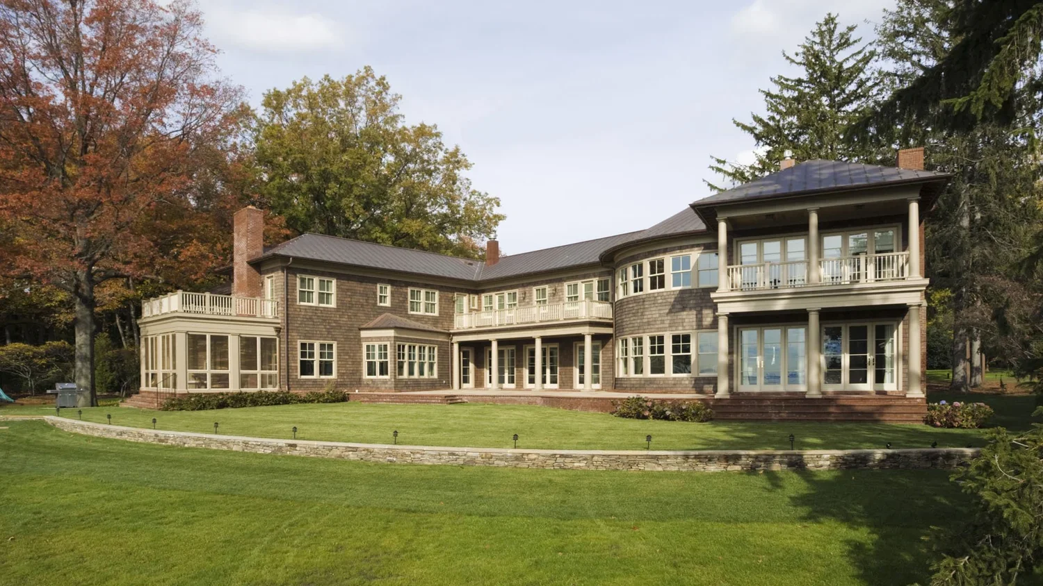 Large modern house with multiple stories and extensive windows, surrounded by green lawn and tall trees.