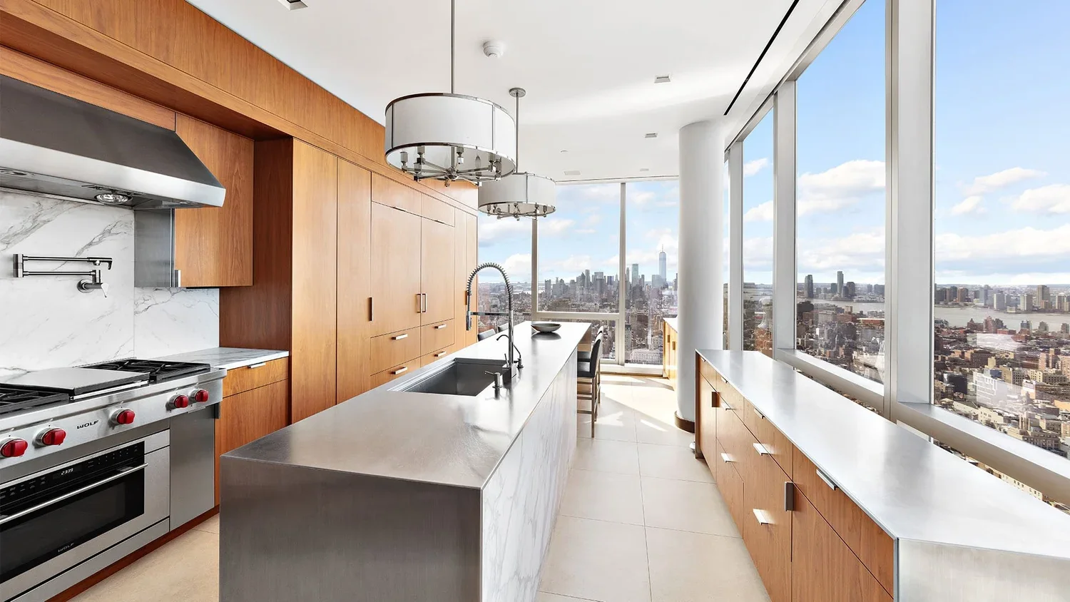 Modern kitchen with wooden cabinets, stainless steel appliances, white marble backsplash, large island with sink, and panoramic city view through floor-to-ceiling windows.