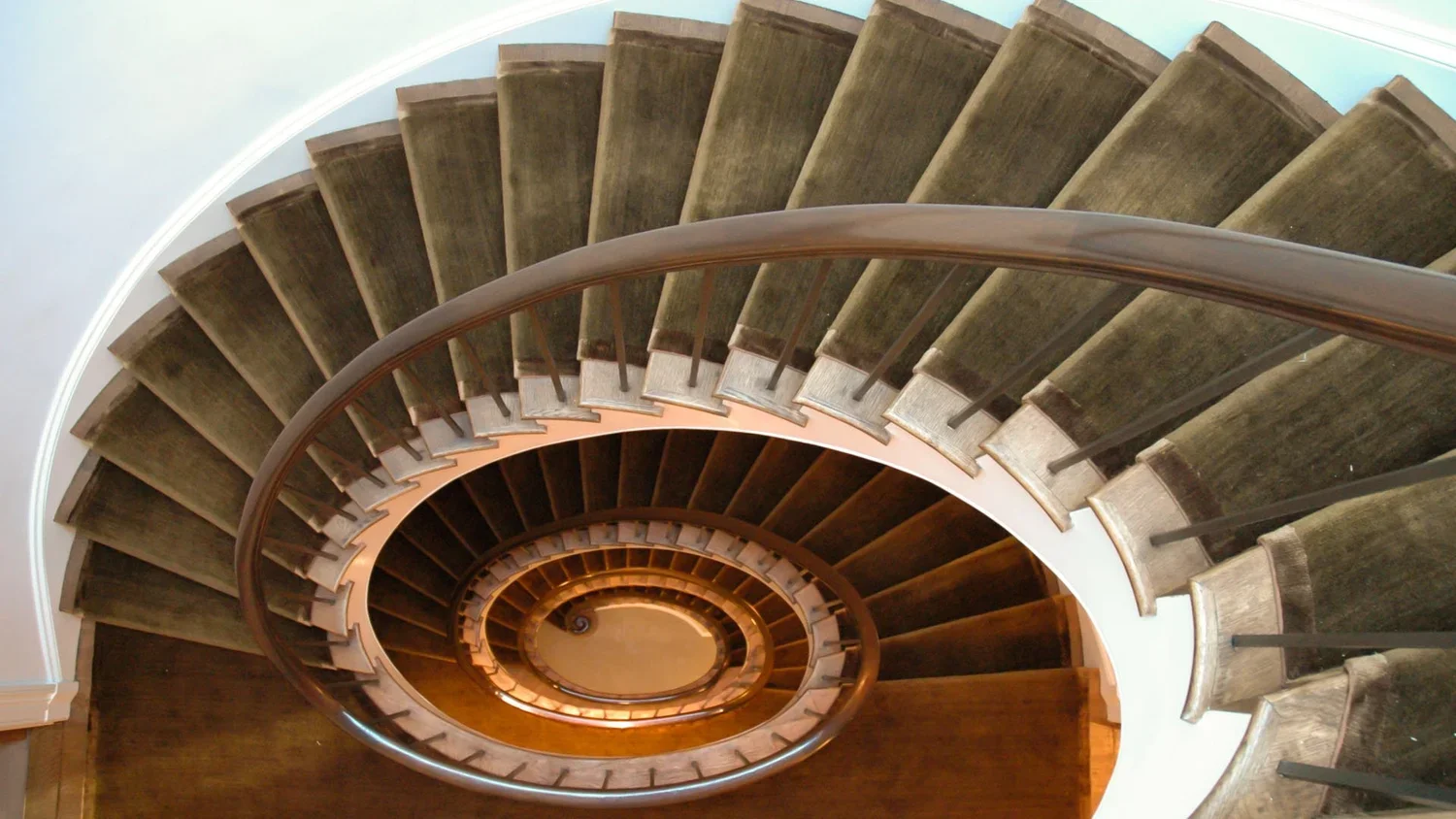 Spiral staircase viewed from above, showcasing wooden steps with a curved handrail.