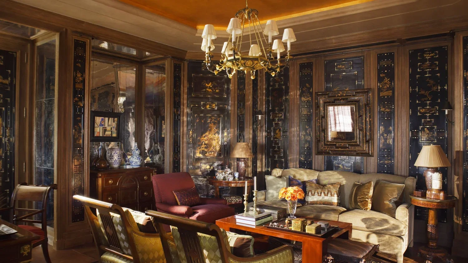 Luxurious living room with ornate wooden paneling, a chandelier, velvet sofas, and decorative lamps.