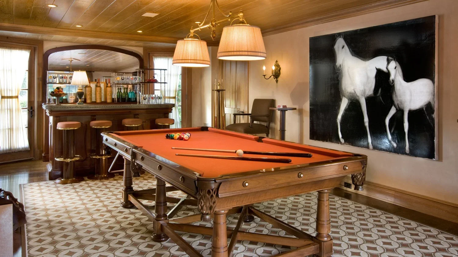 Room with a pool table, bar area, and a large black and white painting of two horses.