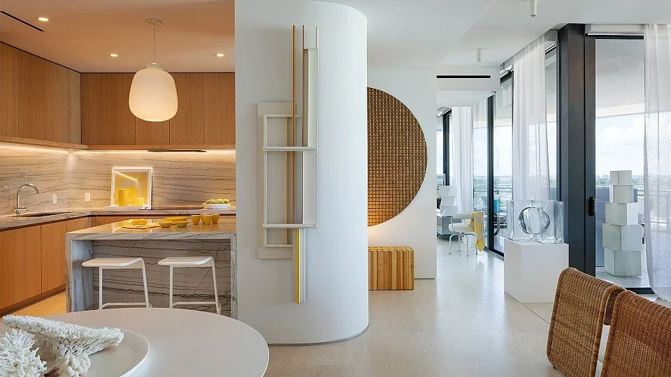 Modern open-concept kitchen and living area with wooden cabinetry, marble countertops, a round dining table, and large windows with sheer curtains letting in natural light.